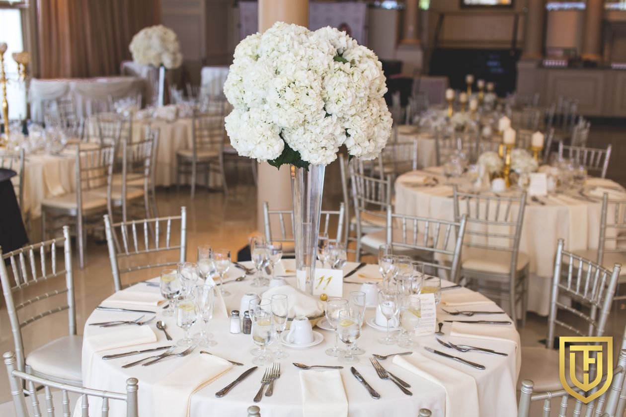 Hotel ballroom set for a banquet with round tables, white linens, and tall floral centerpieces